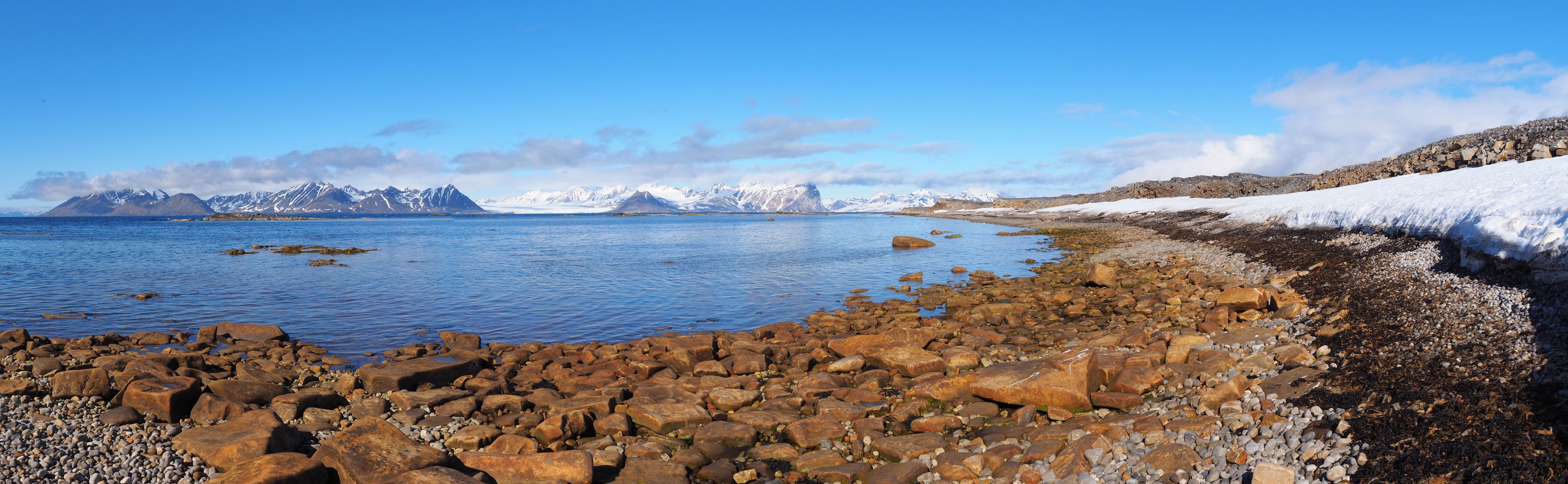 Rocky beach in Svalbard with snowy mountains in the horizon.