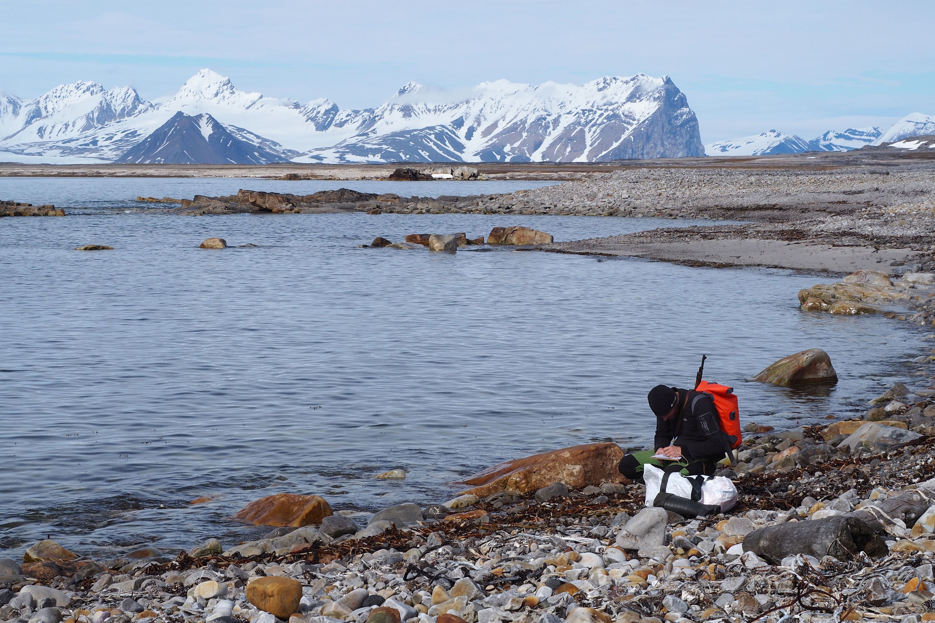 A researcher collecting samples on a rocky beach in Svalbard.